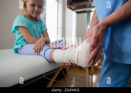 Physiotherapist putting bandage on injured feet of girl patient Stock Photo