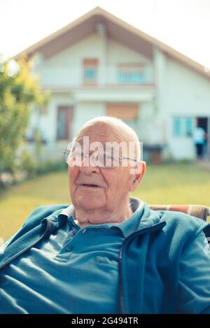 Senior man relaxing sitting in front of his house Stock Photo