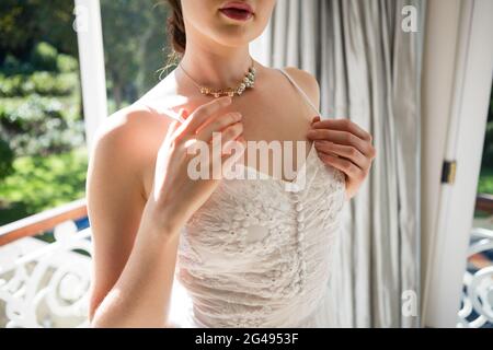 Midsection of bride in wedding dress standing by window Stock Photo