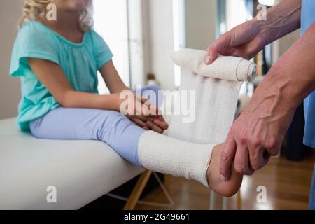 Physiotherapist putting bandage on injured feet of girl patient Stock Photo