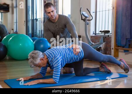 Physiotherapist assisting senior woman in performing exercise on mat Stock Photo