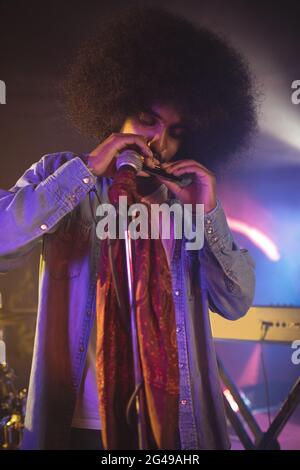 Male musician playing mouth organ in illuminated nightclub Stock Photo