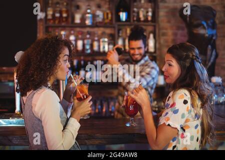 Two young women having cocktail drinks at counter Stock Photo