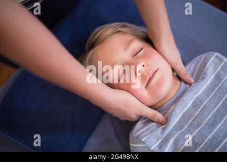 Boy lying with eyes closed receiving neck massage from female therapist Stock Photo