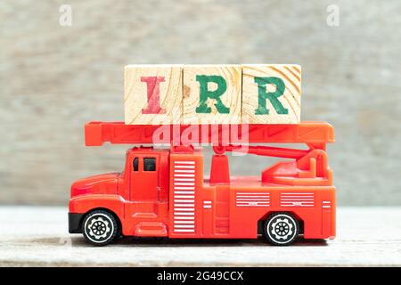 Fire ladder truck hold letter block in word IRR (Abbreviation of internal rate of return) on wood background Stock Photo