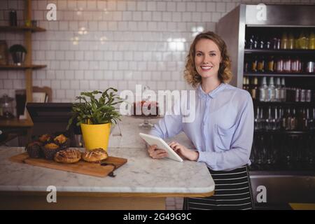 Portrait of attractive young waitress using digital tablet while standing by counter Stock Photo