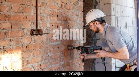 Handyman at a construction site in the process of drilling a wall with an perforator. Stock Photo