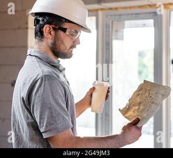An electrician is studying a construction drawing with a coffee in his hand. Stock Photo