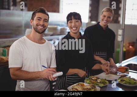 Portrait of waiter with female chefs standing in kitchen Stock Photo