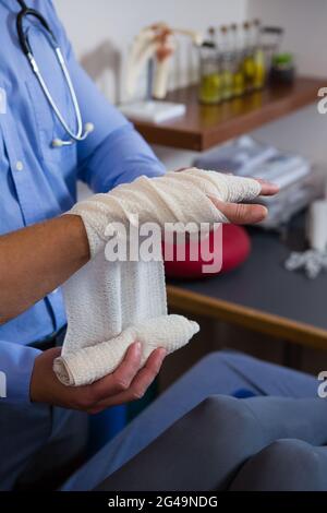 Physiotherapist putting bandage on injured hand of patient Stock Photo