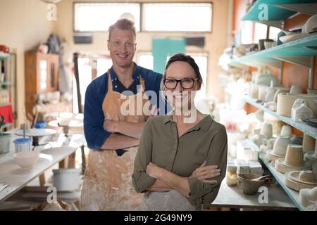 Male and female potter standing with arms crossed in pottery workshop ...