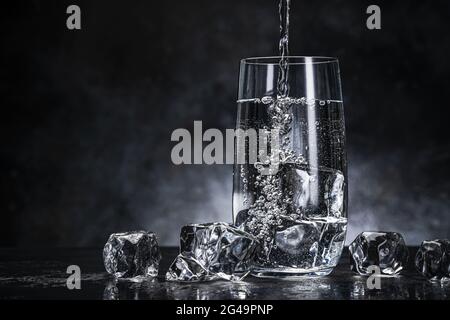 Pouring water from bottle into glass on black background Stock Photo