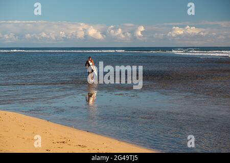 HANALEI, HAWAII, UNITED STATES - Jun 01, 2021: A surfer carries his board out into the water at Ha'ena Beach on Kauai's north shore. Stock Photo