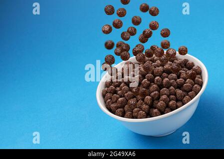 Chocolate Corn balls falling in bowl over blue background Stock Photo