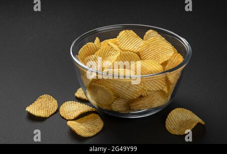 Ridged potato chips in glass bowl on black background Stock Photo