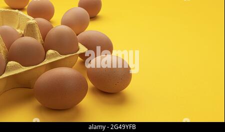 Brown chicken eggs in cardboard box on yellow background Stock Photo