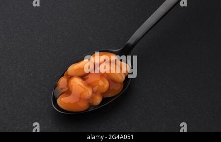 Spoon of baked beans in tomato sauce isolated on black background Stock Photo