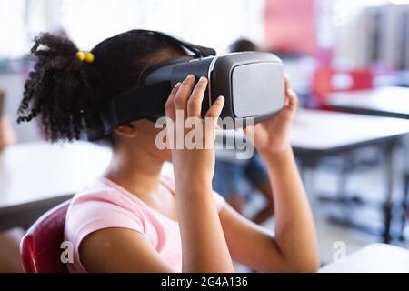 African american girl wearing vr headset while sitting on her desk in the class at school Stock Photo