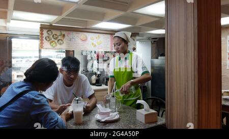 Waitress in Chinese restaurant in Chinatown Bangkok Thailand serving customers sitting at table Stock Photo