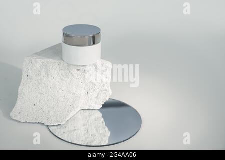 cream box on piece of concrete in cut. Porous structure of concrete is associated with texture of leather. Composition using amirror. Medical cosmetic Stock Photo