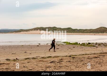Beadnell, Northumberland, UK. 20th June, 2021. A jogger exercises on an empty beach in Beadnell Bay, Northumberland, on a dull morning. Brighter weather is expected later this afternoon. Peter Lopeman/Alamy Live News Stock Photo