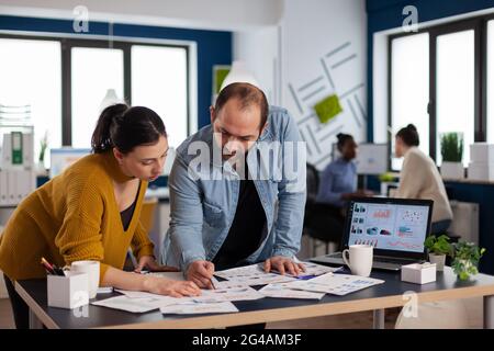 Multi ethnic coworkers team of start up consulting about marketing strategy. Diverse team of business people analyzing company financial reports from computer. Stock Photo