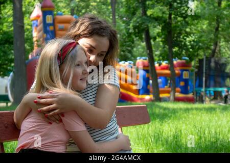 Two sisters in the park near the playground hugging and resting. Girls have fun after a long separation. Stock Photo