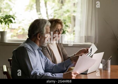 Older couple work with paperwork paying bills online Stock Photo