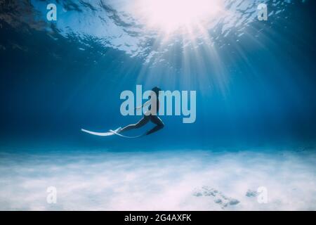 Freediver with white fins glides and posing underwater in ocean with sunlight. Stock Photo