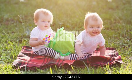 Twin sisters sit on a blanket with a backpack of children's toys. Stock Photo