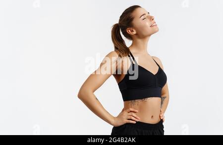 Portrait of fit woman in cheerful mood standing satisfied with hips on body, white isolated background. Smiling female athlete resting after workout Stock Photo