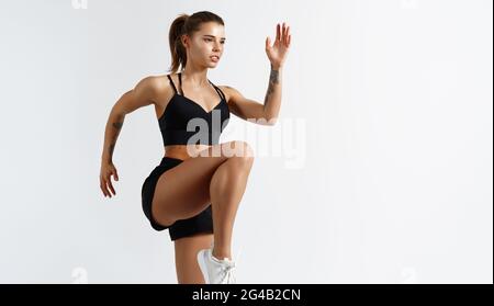 Image of sporty young female athlete, doing leg stretching exercises, lifting legs, dynamic movement training, looking determined, face sweaty during Stock Photo