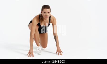 Runner on start. Young woman in low sprint jogging pose, touching ground, ready to run, prepare for running maraphon, looking determined, posing Stock Photo