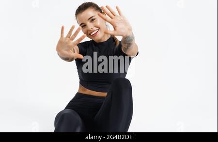 Happy sportswoman sitting on floor in activewear, stretching hands and reaching to camera, waving hands, satisfied with workout, show ten rating Stock Photo