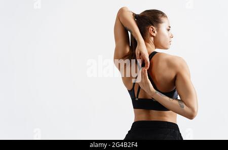 Rear view of fit and sporty fitness woman stretching arms and back before workout exercises. Woman back in black sport clothing standing on white Stock Photo