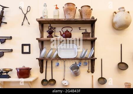 Vejer de la Frontera, Cádiz, Spain - June 14, 2021: Old kitchen utensils on wooden shelves and attached to the wall of a typical Andalusian house in V Stock Photo