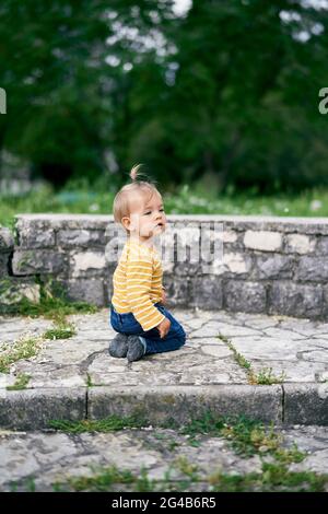 Little girl sits on her knees on stone steps in the park Stock Photo