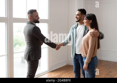 Millennial Couple Buying New Apartment, Shaking Hands With Financial Advisor Stock Photo