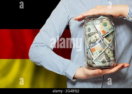 US dollars cash money in glass jar in hand on German flag background. Business, politics, banking and corruption concept Stock Photo