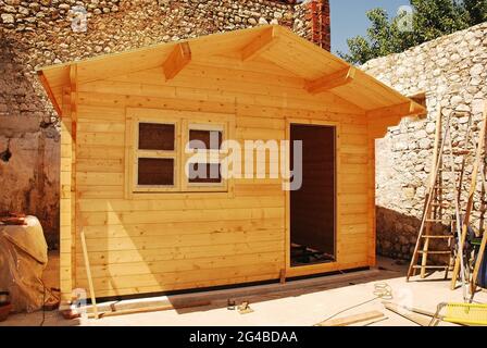 A partially built small prefabricated wooden cabin on a concrete base. The wall beams are in place and the roof is almost complete. Stock Photo