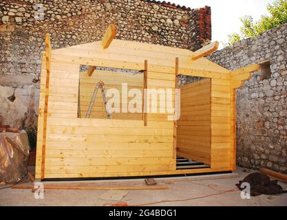 A partially built small prefabricated wooden cabin on a concrete base. The wall beams are in place up to the roof level Stock Photo
