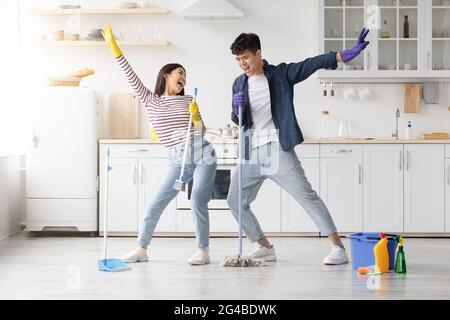 Funny asian couple singing songs while cleaning kitchen, full length Stock Photo