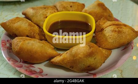 This is an Indian dish called samosa which is served on a white plate with sauce Stock Photo