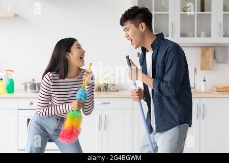 Funny asian man and woman singing songs while house-keeping Stock Photo