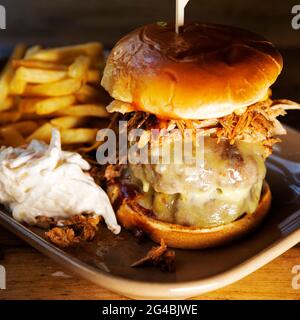 Burger in a brioche bun served with fried and 'slaw. The Burger is topped with melted cheese and shredded pulled pork. Stock Photo
