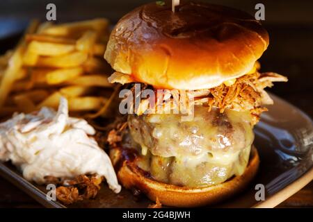 Burger in a brioche bun served with fried and 'slaw. The Burger is topped with melted cheese and shredded pulled pork. Stock Photo
