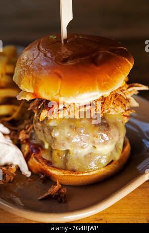 Burger in a brioche bun served with fried and 'slaw. The Burger is topped with melted cheese and shredded pulled pork. Stock Photo