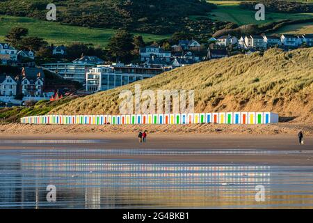 White beach huts, with coloured doors, stand in front of dunes with reflections in the wet beach sand on Woolacombe Beach, Devon Stock Photo