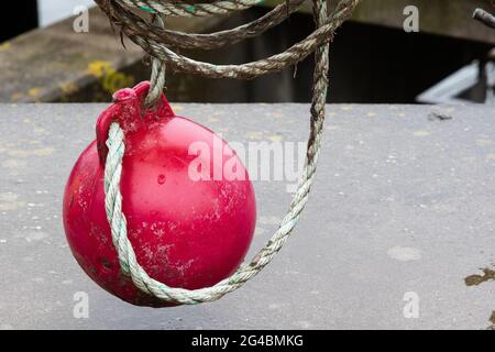 A red round marker buoy hangs from a railing on a coiled rope. Stock Photo