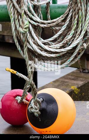 Two round marker buoys in orange and dark red hang on ropes. Stock Photo